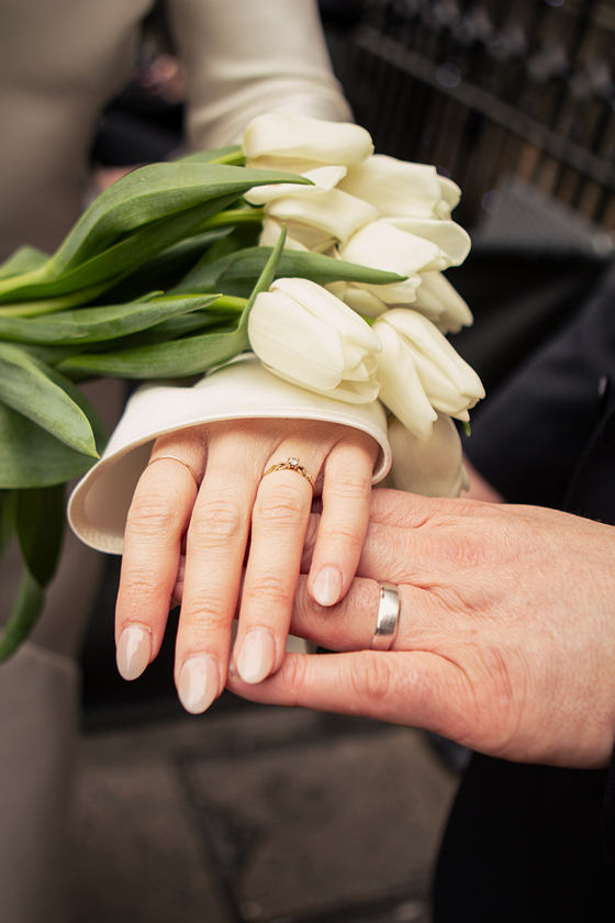 Close-up of a bride and groom showing their wedding rings beside a white tulip bridal bouquet, photographed by Rscott_shoots.