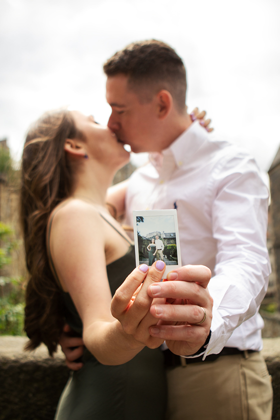 Engaged couple kissing while holding up a Polaroid photograph during a relaxed Edinburgh engagement shoot by Rscott_shoots.