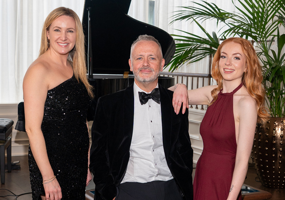 Copper Blonde wedding band trio posing beside a grand piano ahead of a live wedding performance