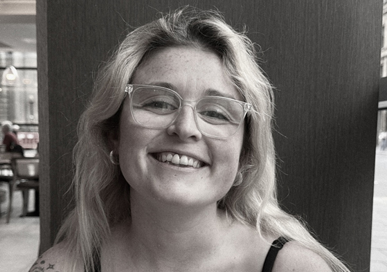 Black-and-white portrait of the smiling With Vic wedding content creator wearing glasses.