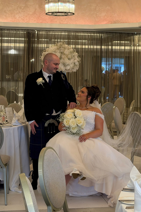 Bride holding a white rose bouquet looks up at the groom during their elegant wedding reception.