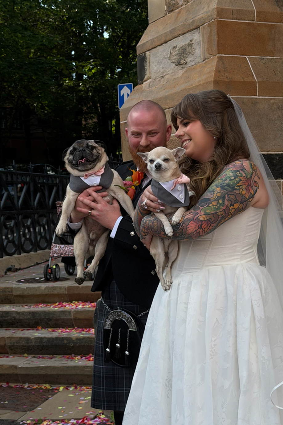 Bride and groom hold their pug and Chihuahua dressed in matching outfits outside their wedding ceremony.