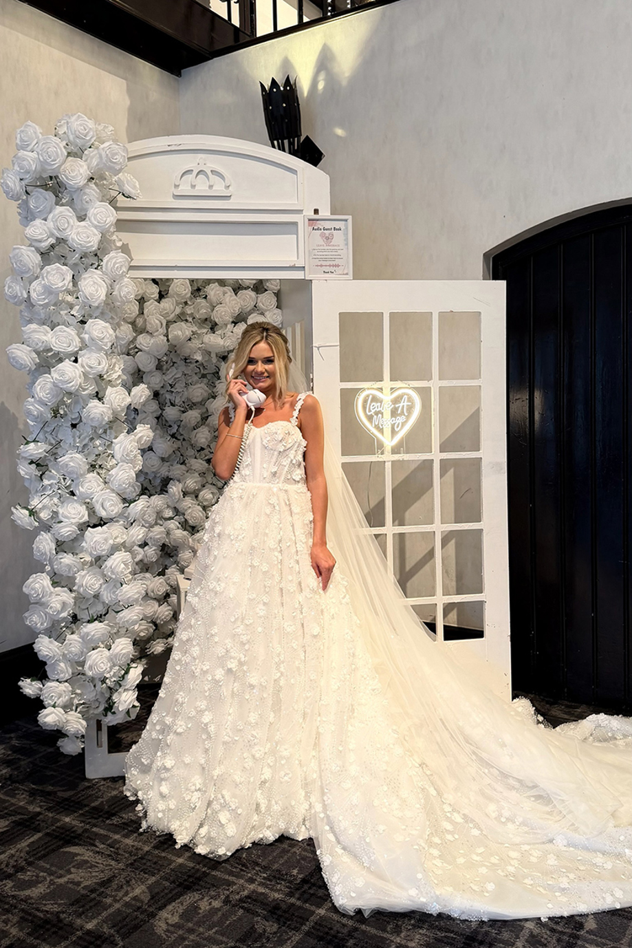 Bride uses a telephone audio guest book surrounded by white rose decorations at her wedding reception.