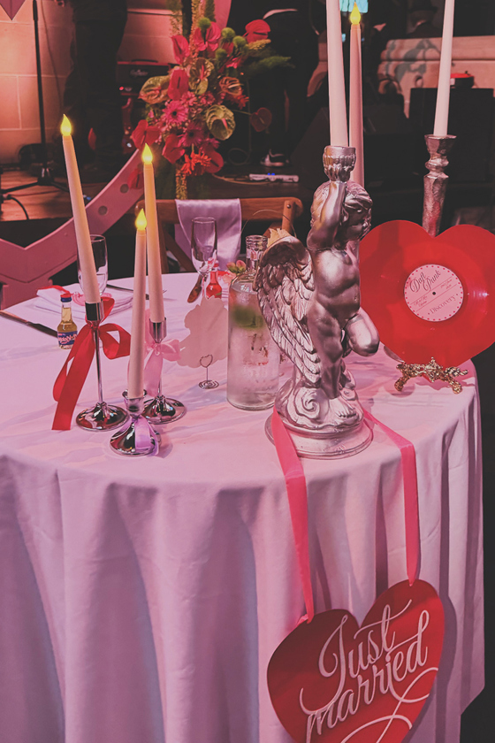 Red-themed wedding reception table styled with taper candles, colourful flowers, vinyl décor and a Just Married sign.