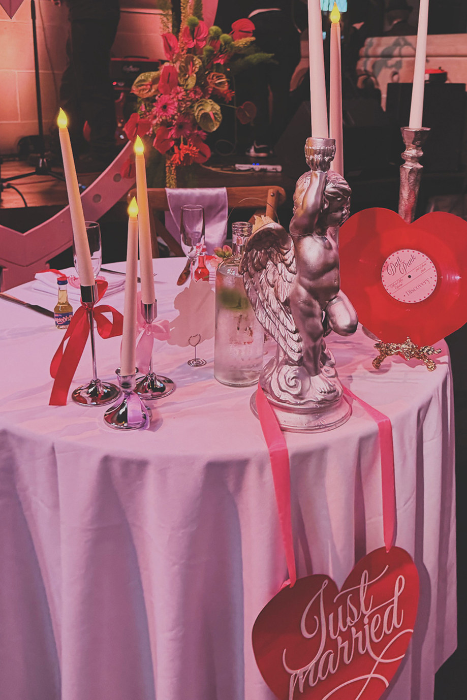 Red-themed wedding reception table styled with taper candles, colourful flowers, vinyl décor and a Just Married sign.
