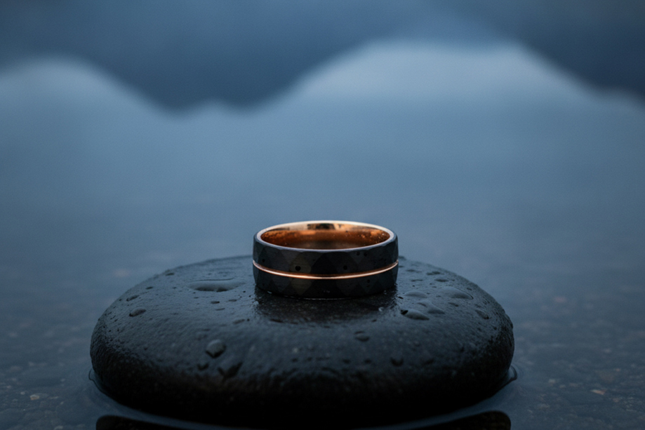 Dark Forge & Lumber Foundry wedding band with copper detailing displayed on a rain-covered stone overlooking a Scottish loch.