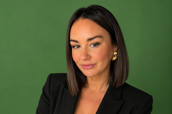 Portrait of Leah from Browz & Bronze by Leah wearing a black blazer against a green background.