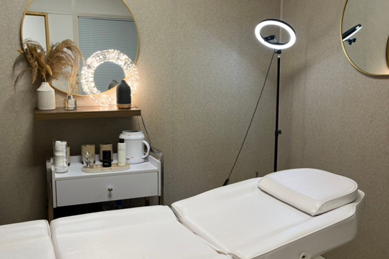 Browz & Bronze by Leah beauty treatment room with reclining bed, skincare products, mirrors and ring light.