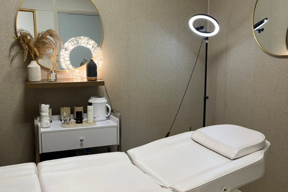 Browz & Bronze by Leah beauty treatment room with reclining bed, skincare products, mirrors and ring light.