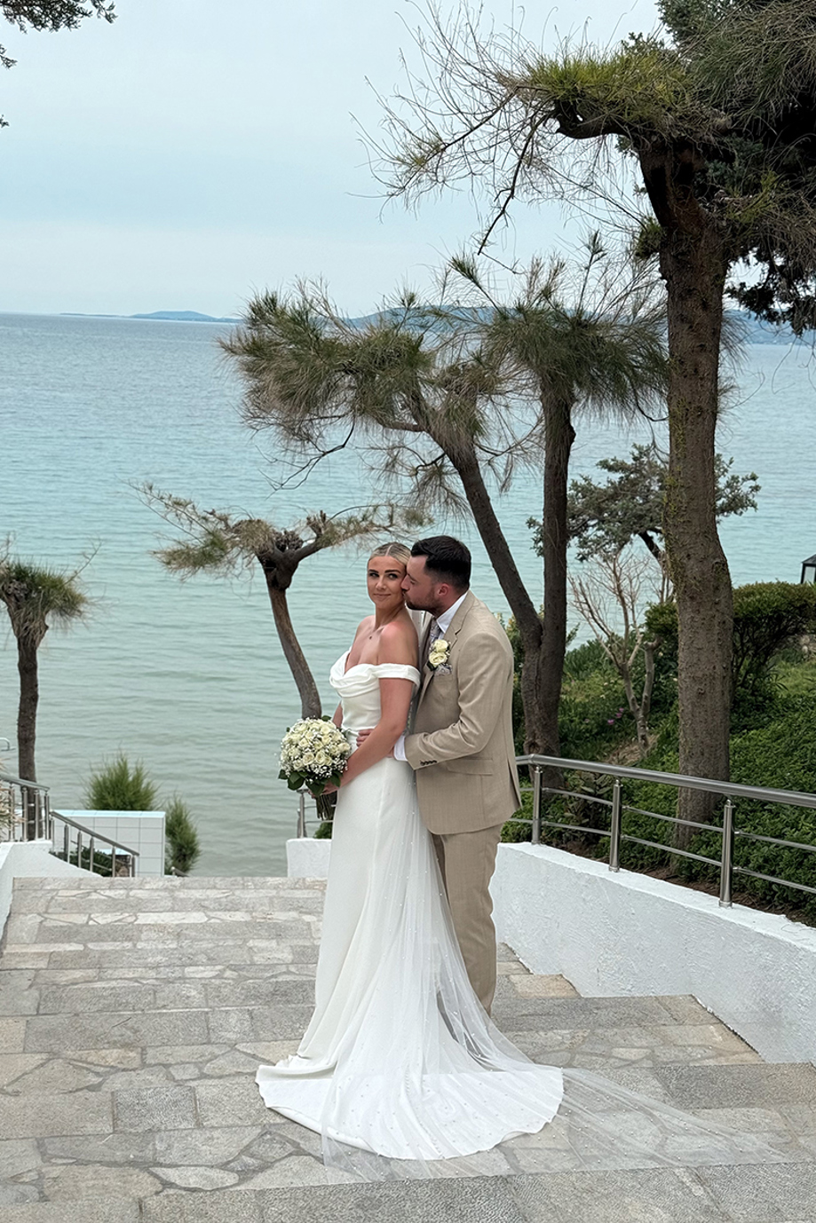 Groom kisses the bride beside the sea during an outdoor destination wedding portrait.