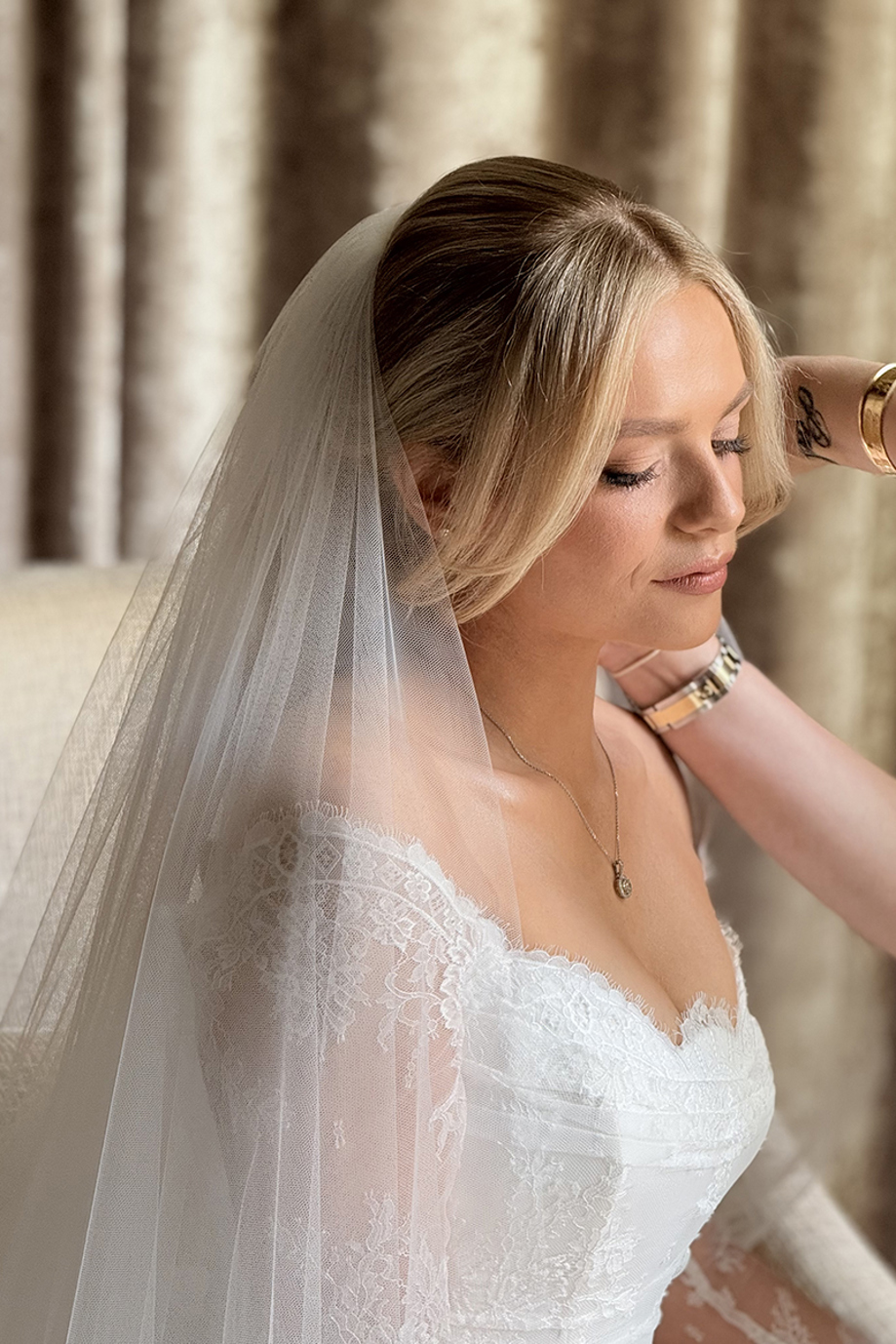 Close-up of a bride in a lace wedding dress having her veil adjusted before the ceremony.