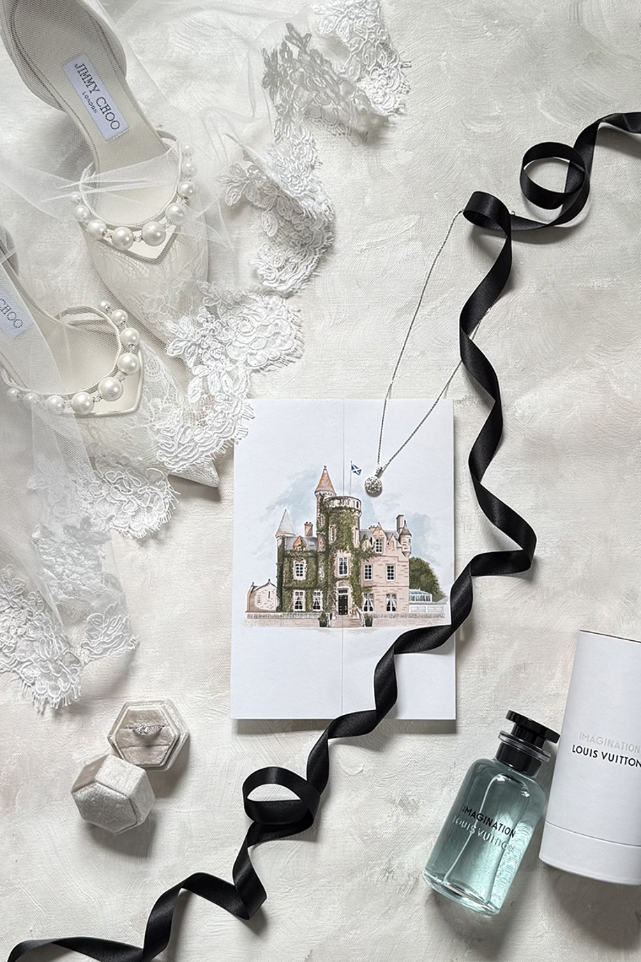 Luxury wedding details flat lay featuring Jimmy Choo bridal shoes, lace veil, rings, jewellery, perfume and venue stationery.