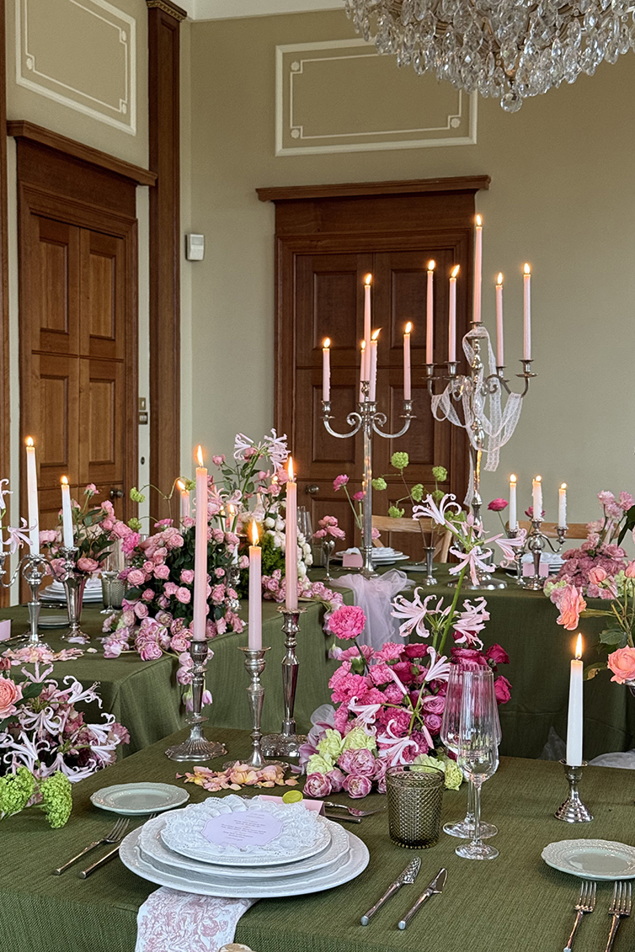 Wedding reception tables styled with green tablecloths, pink flowers, silver candlesticks and glowing taper candles.