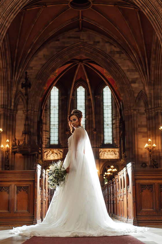 Bride carries a loose white and green bouquet by Maison Bloom Florals inside a grand Gothic wedding chapel.
