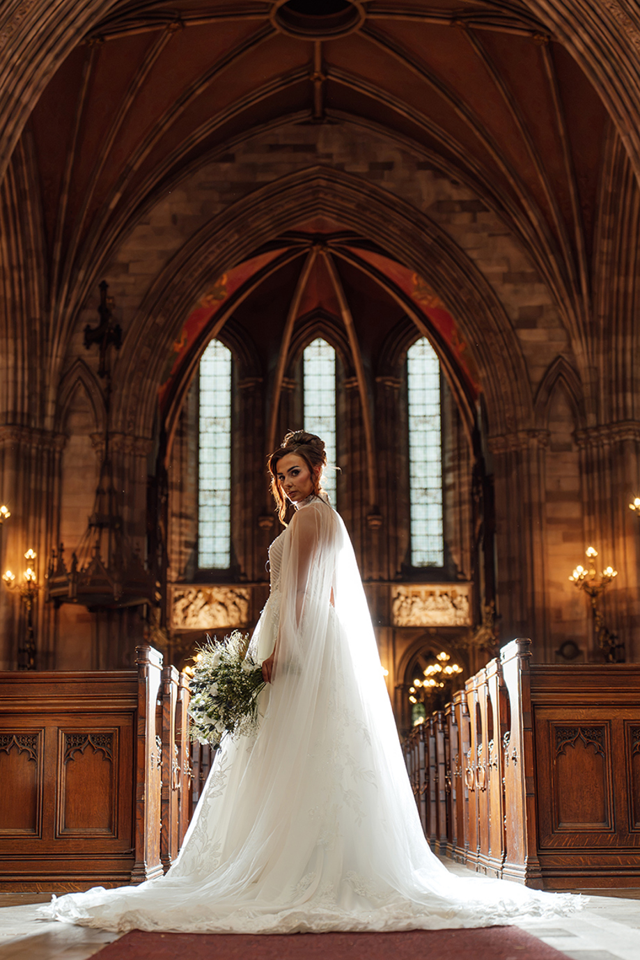 Bride carries a loose white and green bouquet by Maison Bloom Florals inside a grand Gothic wedding chapel.