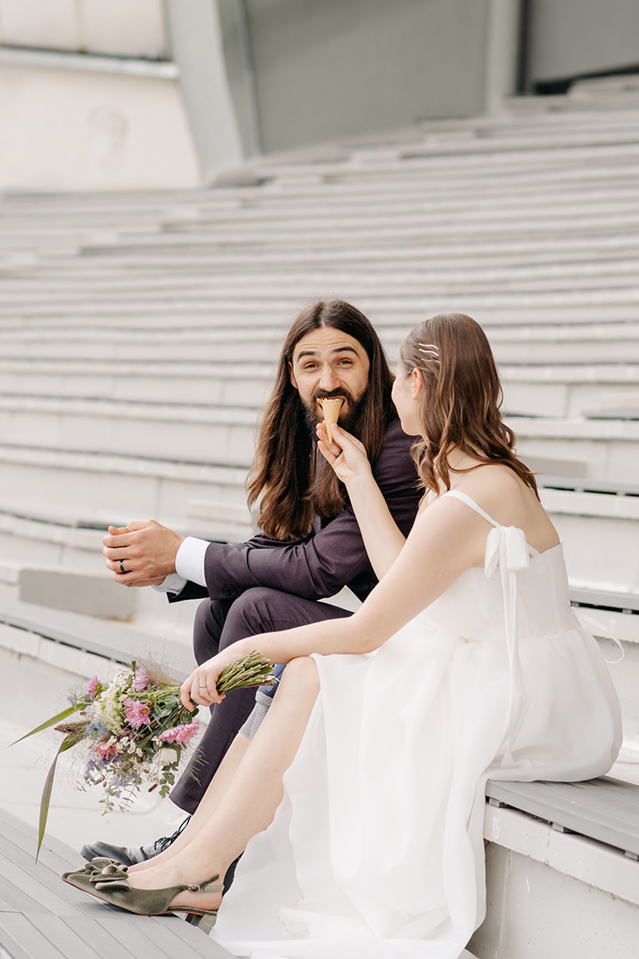 Relaxed wedding portrait by Goda and Justas Photography of a bride feeding her groom ice cream as they sit together on outdoor steps.