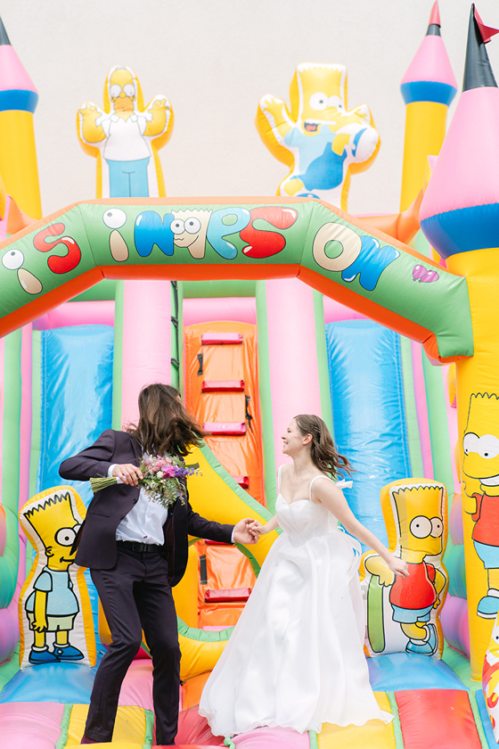 Newlywed couple having fun on a colourful Simpsons-themed wedding bouncy castle, photographed by Goda and Justas Photography.