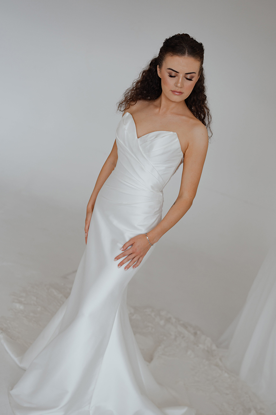 Bride in a one-shoulder satin wedding dress with curly half-up hair and polished bridal makeup by Bridal by Regina.