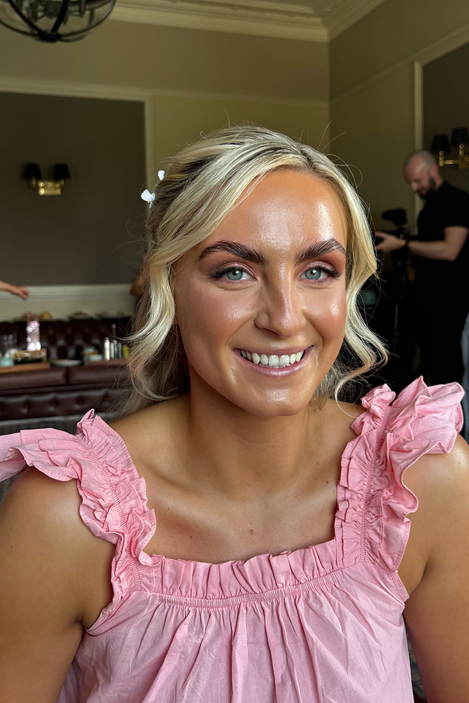Smiling bridal party member in a pink dress with glowing makeup and blonde updo styled by Bridal by Regina.