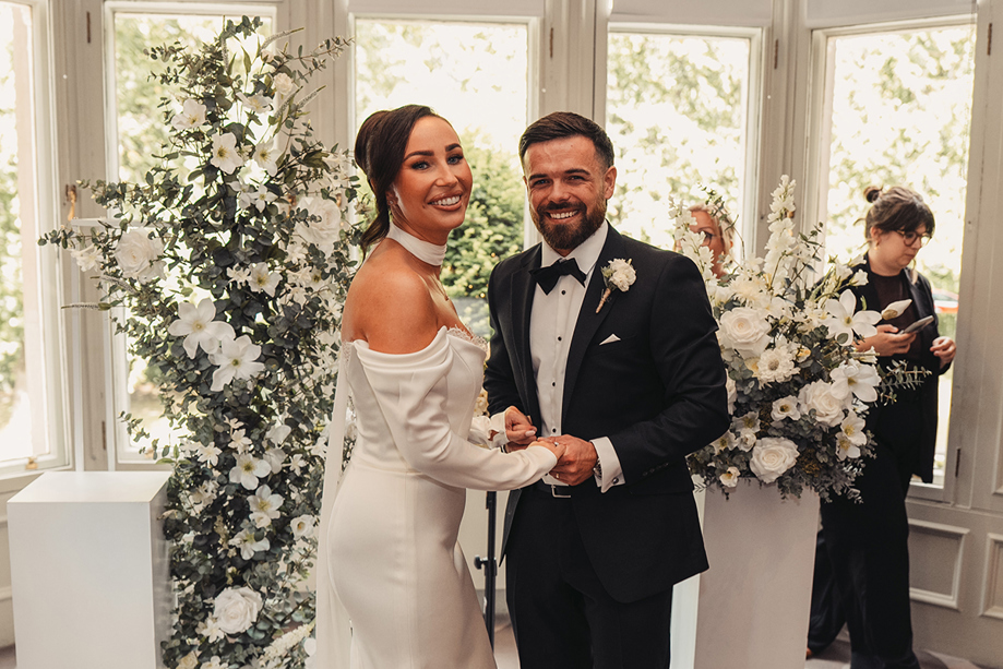 Bride and groom smile together after their wedding ceremony, led by Fiona MacAlister Celebrant and surrounded by white floral arrangements.