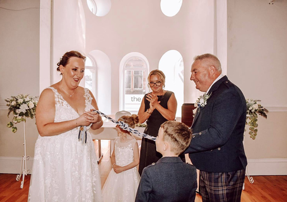 Bride and groom take part in a symbolic handfasting ceremony with their children and Fiona MacAlister Celebrant.