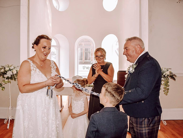 Bride and groom take part in a symbolic handfasting ceremony with their children and Fiona MacAlister Celebrant.