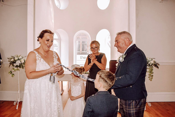 Bride and groom take part in a symbolic handfasting ceremony with their children and Fiona MacAlister Celebrant.