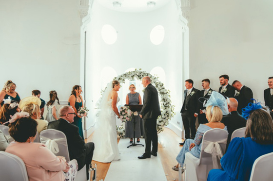Bride and groom exchange vows beneath a white floral hoop during a wedding ceremony conducted by Fiona MacAlister Celebrant.