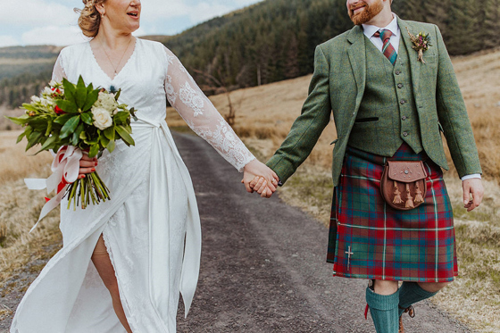 Close-up view of bride and groom walking through Scottish countryside, highlighting traditional wedding kilt styling.