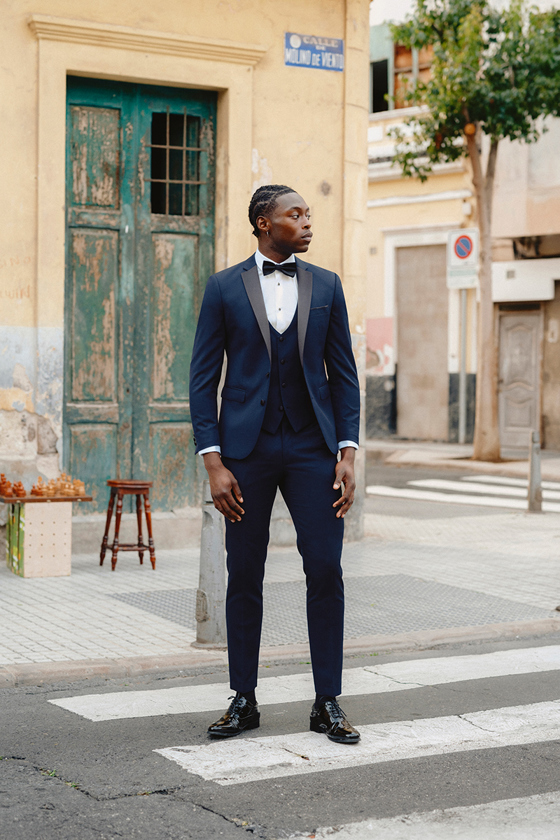 Man in three-piece navy tuxedo with black bow tie on zebra crossing