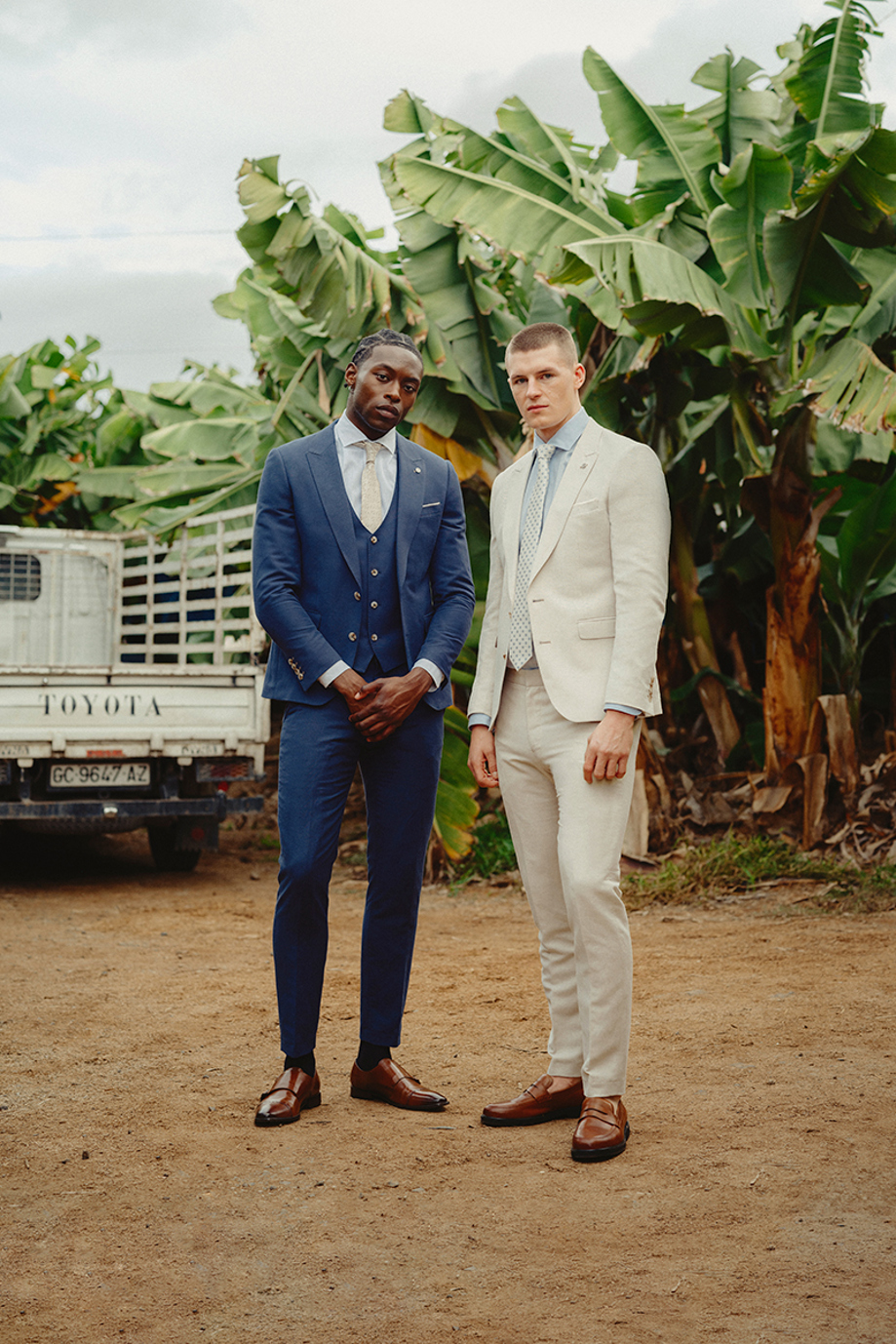 Two men in suits, beige and navy, in Gran Canaria in front of tropical trees