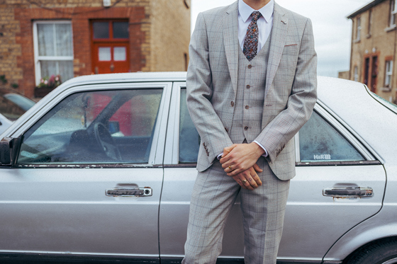 Body of man in three-piece suit standing in front of silver car