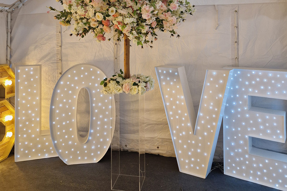 Letter lights saying "Love" with acrylic pillar topped with pink and white floral tree
