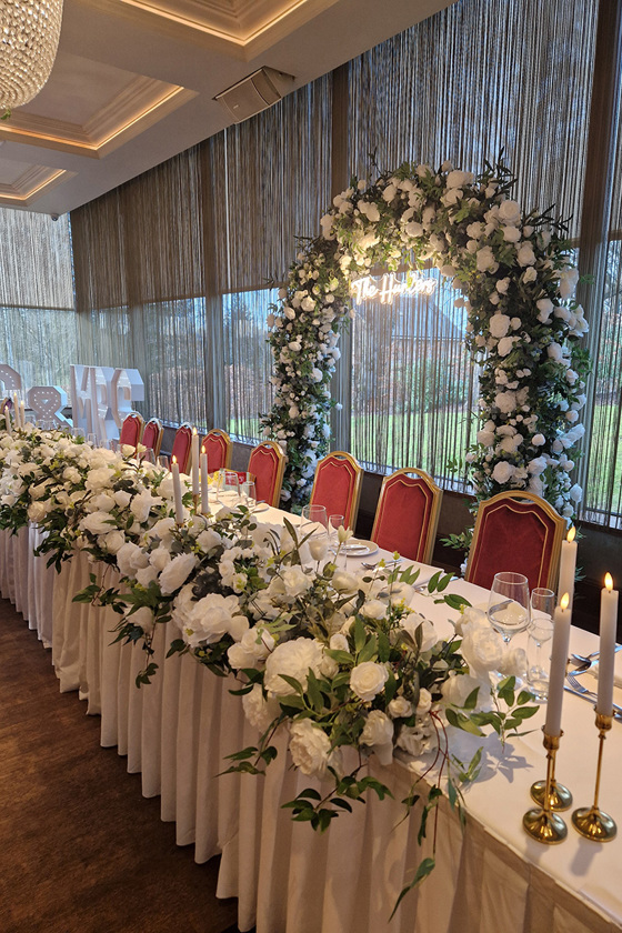 Floral arch with bouquet-covered top table and Mrs & Mrs lights in background