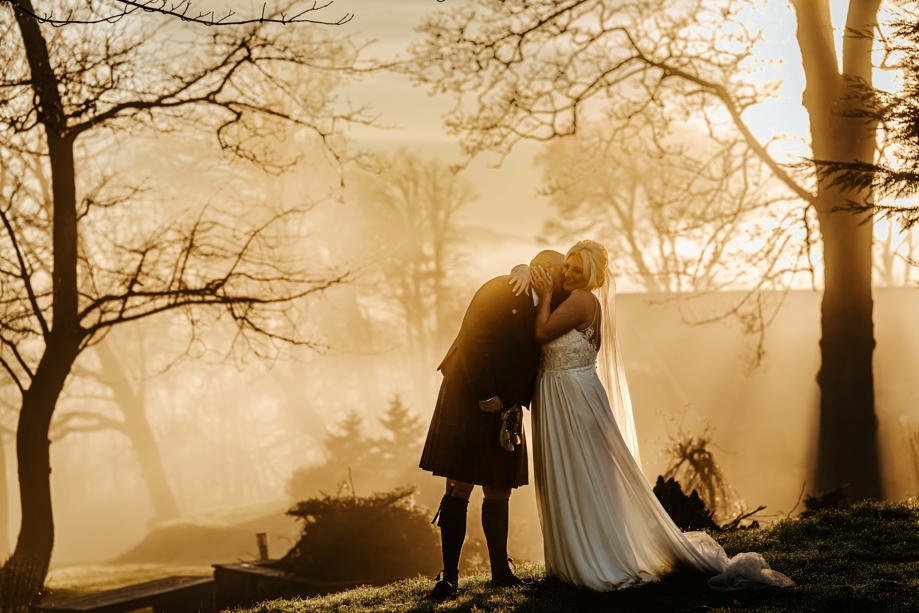 Groom kisses his bride at sunset in the trees