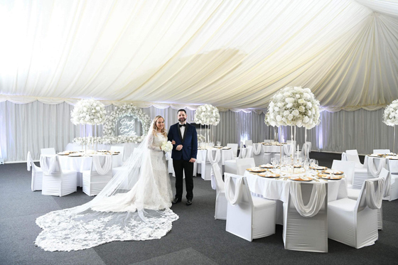 Bride and groom pose in meal set-up at Geilsland Estate, with white roses and draped ceiling.