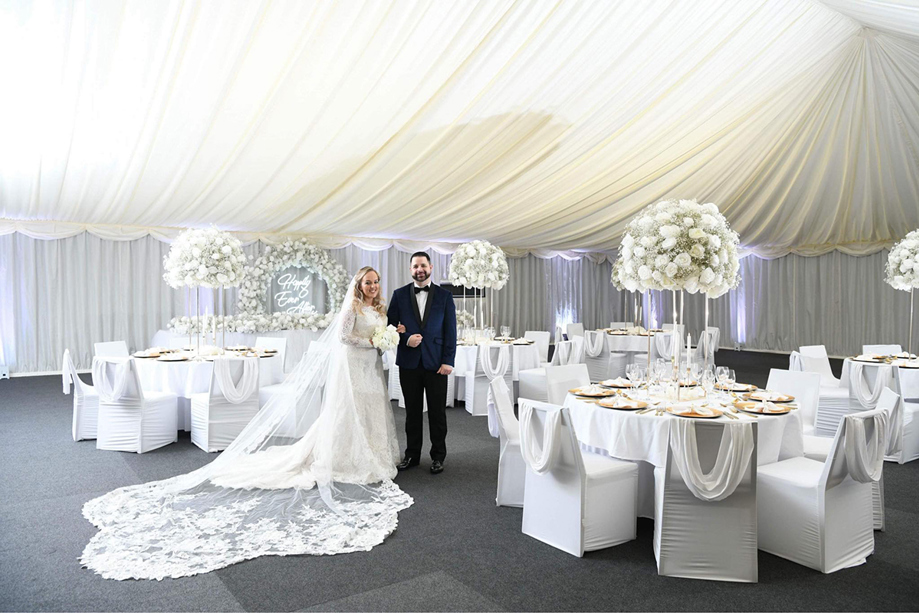 Bride and groom pose in meal set-up at Geilsland Estate, with white roses and draped ceiling.
