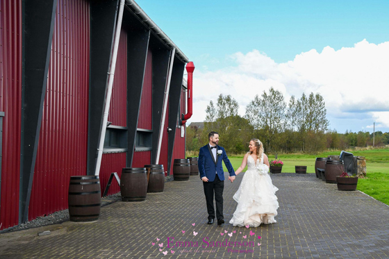 Bride and groom walk hand in hand along side of barn wedding space at Geilsland Estate.