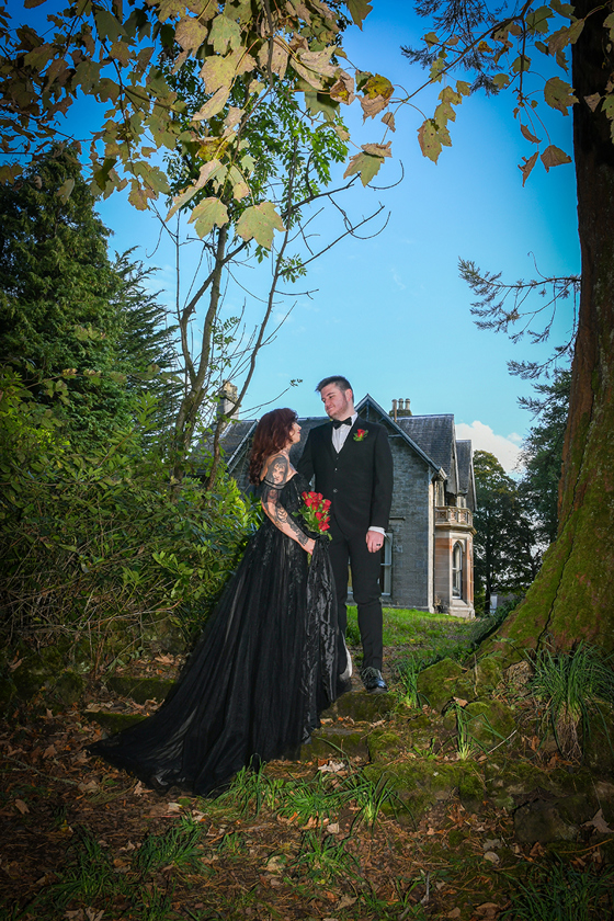 Bride and groom wearing black pose on grounds of Geilsland Estate.