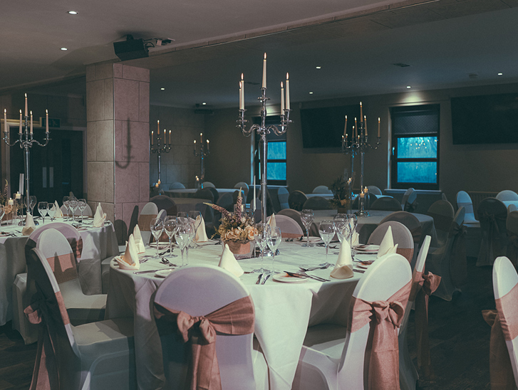 Wedding meal set up in the Crosslee Suite at The River Inn in Houston, Renfrewshire, with pink bows on chairs and silver candelabras.