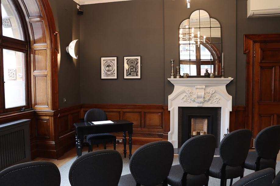 White fireplace in room with dark walls and black chairs set up for a ceremony.