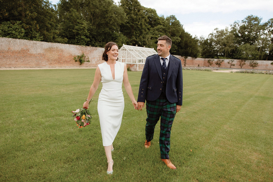 Bride and groom laugh as they walk hand-in-hand across the lawns of the 18th-century Walled Garden at Newton Don.