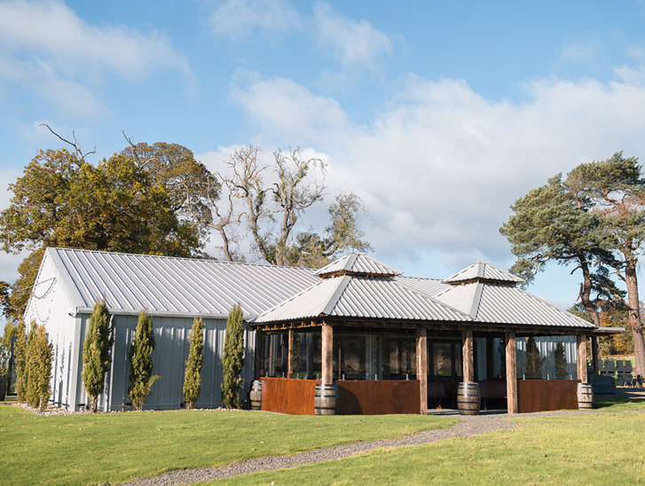 Exterior corner view of The Venue @ Duntarvie Castle in West Lothian, showing contemporary barn-style wedding venue surrounded by countryside and mature trees.