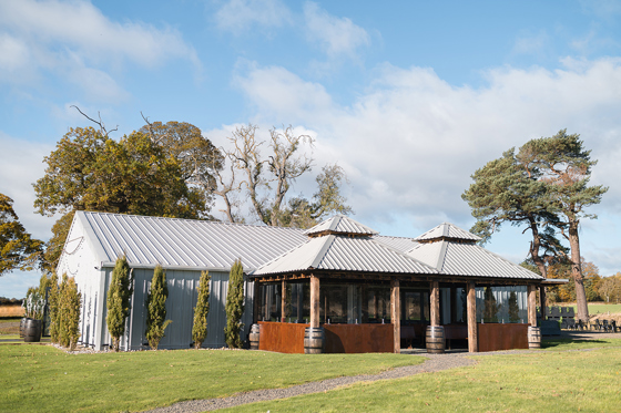 Exterior corner view of The Venue @ Duntarvie Castle in West Lothian, showing contemporary barn-style wedding venue surrounded by countryside and mature trees.
