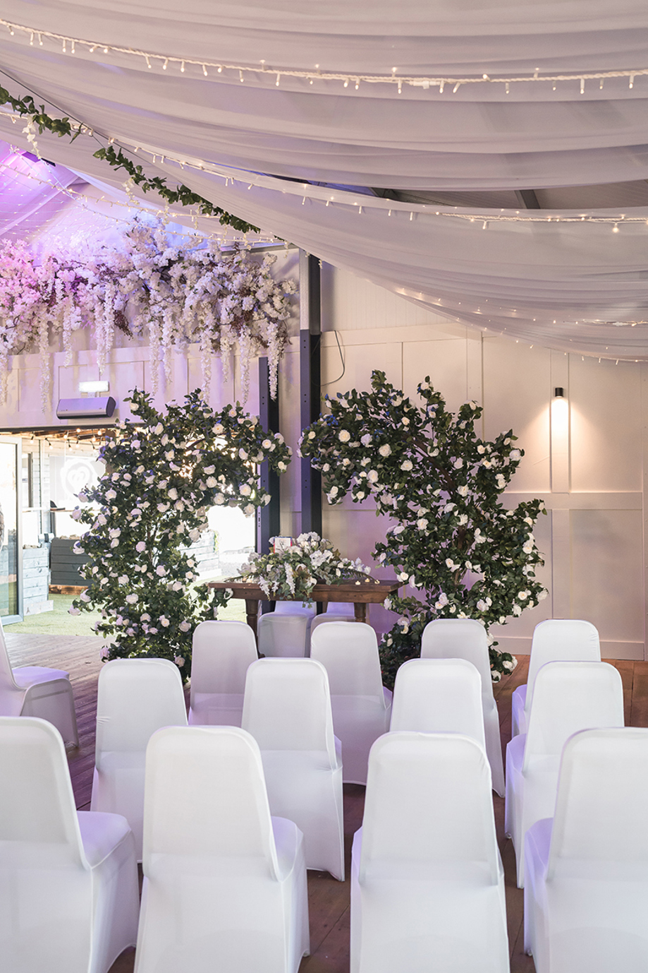 Indoor wedding ceremony setup at The Venue @ Duntarvie Castle with draped white ceiling, fairy lights, floral installations and elegant aisle seating.