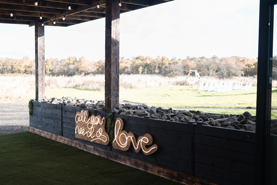 Outdoor wedding ceremony area at The Venue @ Duntarvie Castle with wooden structure and neon “All You Need Is Love” sign overlooking Scottish countryside.