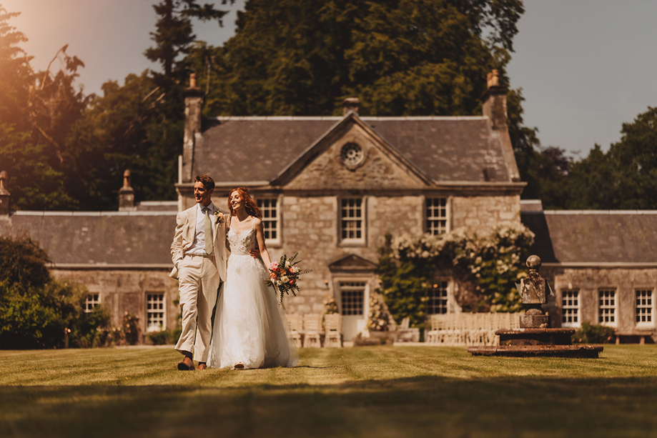 Newlyweds walking through the gardens at Broomholm Manor during a summer wedding in Dumfriesshire.