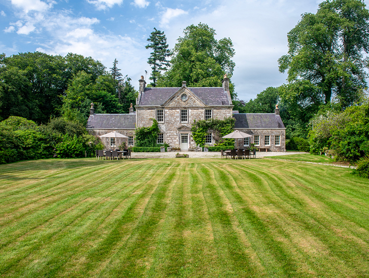 Exterior of Broomholm Manor surrounded by lawns, mature trees and private grounds in the Scottish Borders.