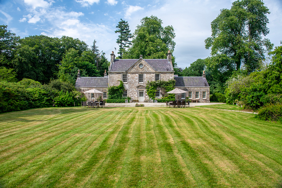 Exterior of Broomholm Manor surrounded by lawns, mature trees and private grounds in the Scottish Borders.