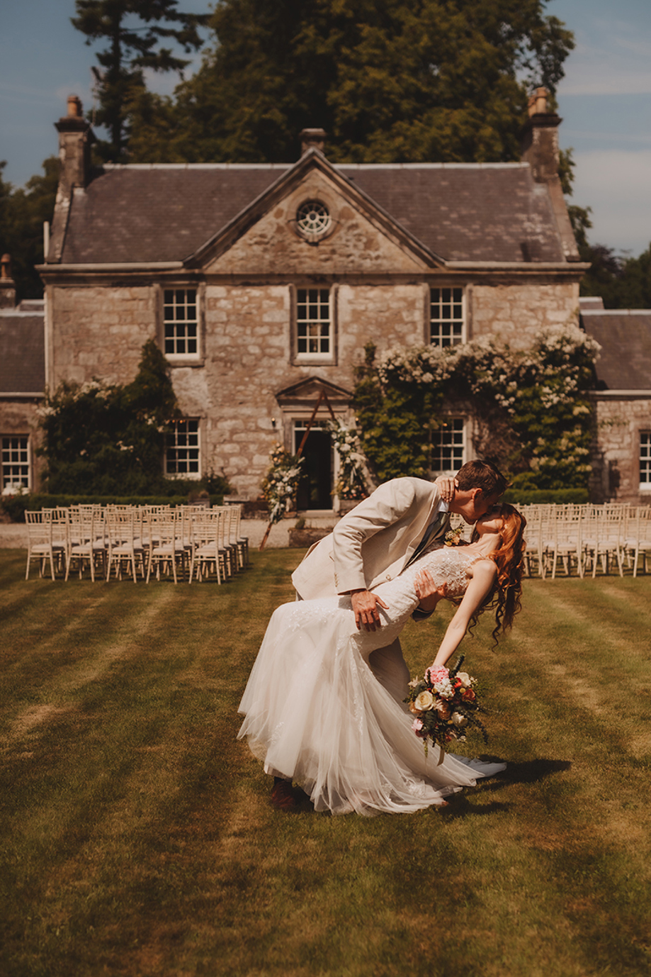 Bride and groom posing in front of Broomholm Manor after an outdoor wedding ceremony on the lawn.